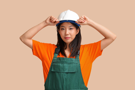 Asian woman in jumpsuit and hardhat on beige backgroundの写真素材
