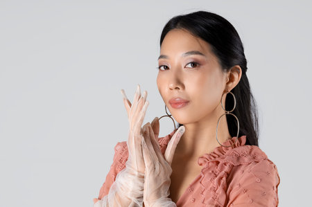 Young Asian woman in gloves with earrings on white backgroundの写真素材