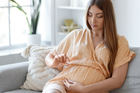 Young pregnant woman with pill sitting at homeの写真素材