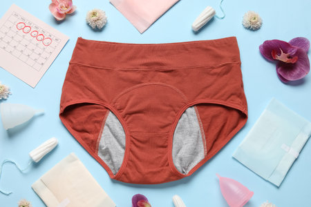 Composition with period panties, pads, tampons, menstrual cup and beautiful flowers on blue backgroundの写真素材