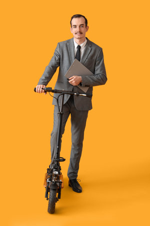 Handsome businessman with clipboard and kick scooter on yellow backgroundの写真素材