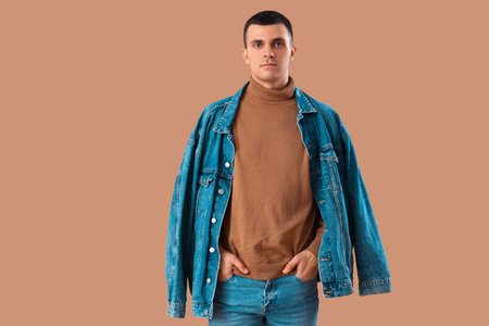 Stylish young man in denim jacket on brown background
