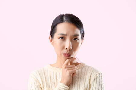 Portrait of thoughtful young Asian woman on pink backgroundの写真素材