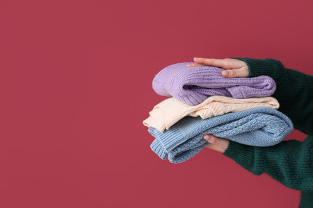 Woman holding stack of different stylish sweaters on burgundy backgroundの写真素材