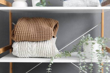 Shelving unit with stack of sweaters and houseplant near gray stylish wall in room, closeupの写真素材