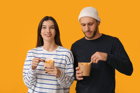 Beautiful young couple with French fries on yellow background