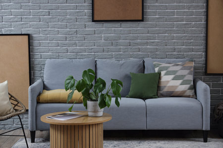 Interior of modern living room with cozy gray sofa and coffee table near brick wall