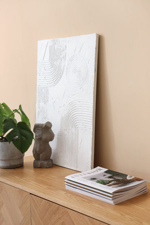 Wooden sideboard with houseplant, magazines and decor near beige wall