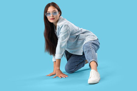 Stylish young Asian woman in sunglasses and denim clothes on blue background