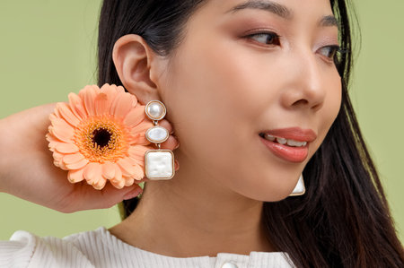 Young Asian woman with beautiful earrings and flower on light green background
