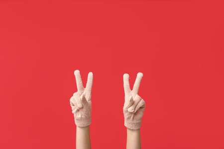 Hands in warm gloves showing victory gestures on red backgroundの写真素材