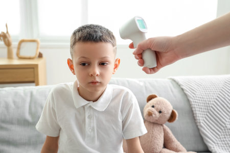 Woman with infrared thermometer measuring temperature of ill little boy at home, closeupの写真素材