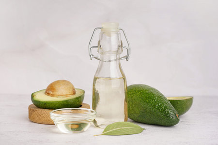 Fresh avocados, glass bottle and bowl with essential oil on white grunge background