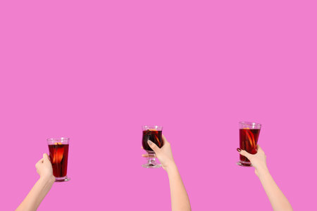 Female hands with glasses of warm mulled wine on pink backgroundの写真素材