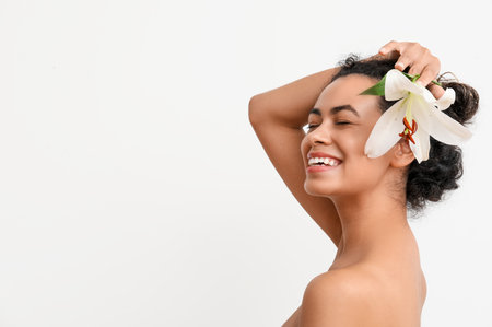 Beautiful young African-American woman with lily flower on white backgroundの写真素材