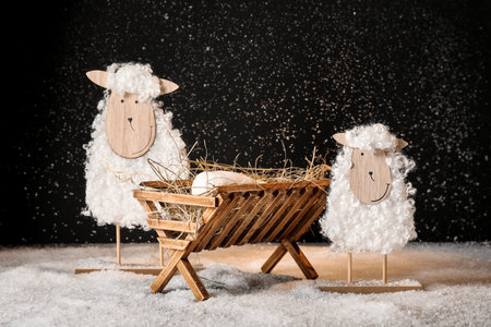 Toy sheep and wooden manger with dummy of baby on snow against black background. Concept of Christmas storyの写真素材