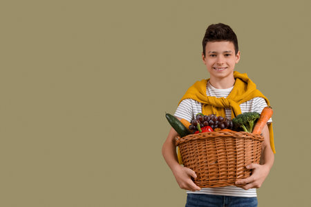 Cute little boy holding wicker basket with different vegetables on green backgroundの写真素材