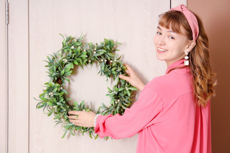Woman in pink shirt hanging Christmas mistletoe wreath on doorの写真素材