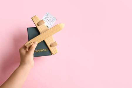 Female hand with wooden plane, passport and ticket on pink backgroundの写真素材