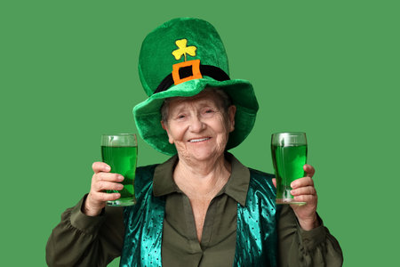 Senior woman in leprechaun hat with glasses of beer on green background. St. Patrick's Day celebrationの写真素材