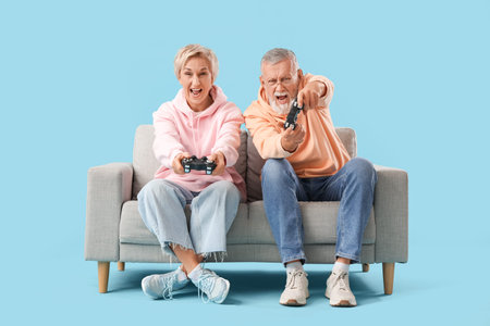 Mature couple playing video game on sofa against blue background