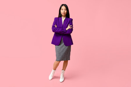 Portrait of young Asian businesswoman with crossed arms on pink backgroundの写真素材