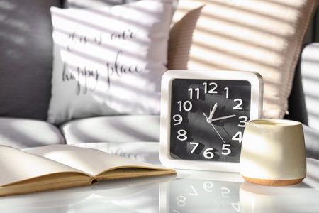 Modern clock, candle and notebook on table in room
