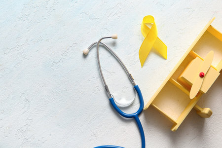 Golden ribbon with stethoscope and toy on light blue background. Children cancer awareness conceptの写真素材
