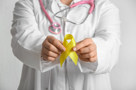 Doctor holding golden ribbon on white background, closeup. Childhood cancer awareness conceptの写真素材