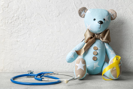 Golden ribbon with stethoscope and toy bear on grunge background. Children cancer awareness conceptの写真素材