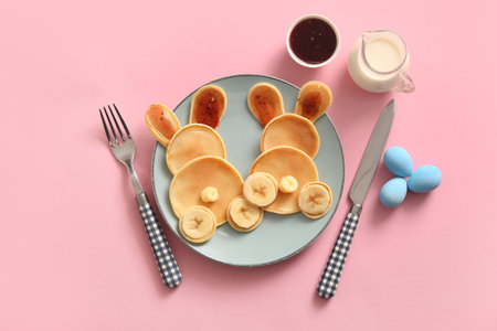 Funny Easter bunny pancakes with banana and painted eggs on pink backgroundの写真素材
