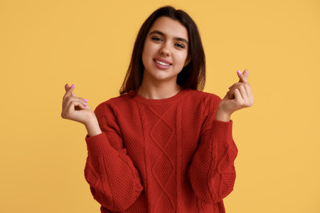 Happy young girl showing heart gesture on yellow background. Valentine's Day celebrationの写真素材