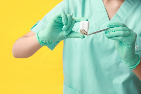 Female dentist with tool and plastic tooth on yellow background. World Dentist Dayの写真素材