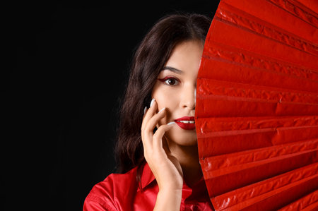 Beautiful young Asian woman with fans on black background. Chinese New Year celebrationの写真素材