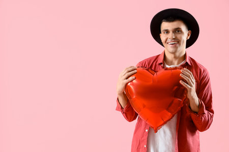 Handsome man with heart-shaped balloon on pink background. Valentine's Day celebrationの写真素材