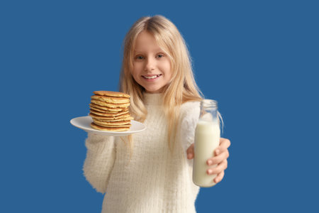 Little girl with tasty pancakes and bottle of milk on blue backgroundの写真素材