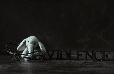 Toy elephant with barbed wire and word VIOLENCE on dark backgroundの写真素材