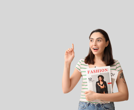 Beautiful woman with magazines pointing at something on light backgroundの写真素材
