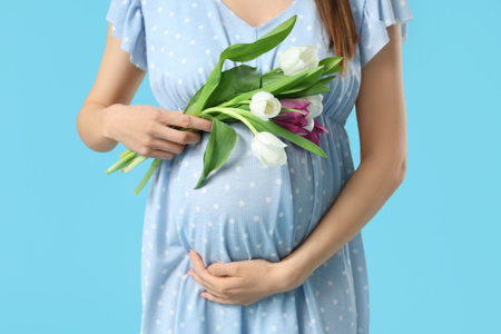 Young pregnant woman with bouquet of tulips on blue background. International Women's Dayの写真素材