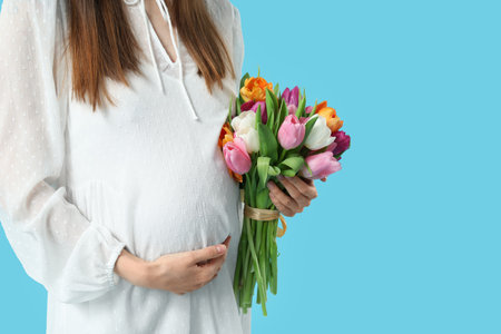 Young pregnant woman with bouquet of tulips on blue background. International Women's Dayの写真素材