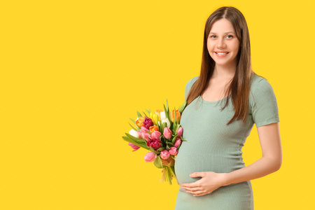 Beautiful young pregnant woman with bouquet of tulips on yellow background. International Women's...
