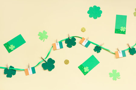 Paper garland with clover and Irish flags for St. Patrick's Day celebration on beige background