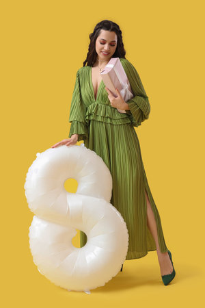 Beautiful woman with gift and balloon in shape of figure 8 on yellow background. International...