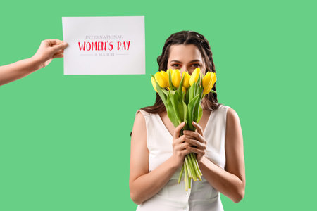 Beautiful woman with tulips and card on green background. International Women's Dayの写真素材