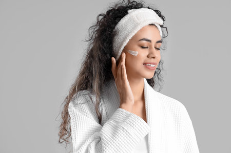 Young African-American woman applying facial cream on light background, closeupの写真素材