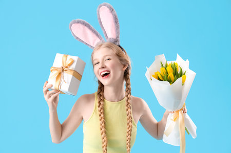 Young girl with Easter gift, flowers and bunny ears on blue backgroundの写真素材