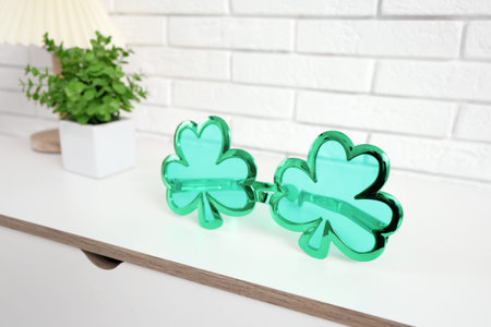 Clover shaped novelty glasses on white chest of drawers, closeup. St. Patrick's Day celebration