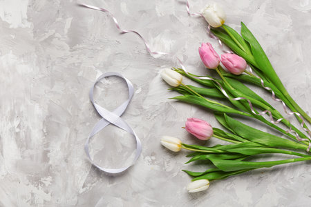 Figure 8 made of ribbon and tulip flowers on gray grunge background. International Women's Day celebrationの写真素材