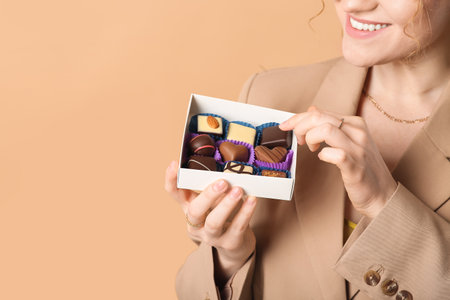 Young woman holding box with sweet chocolate candies on brown backgroundの写真素材
