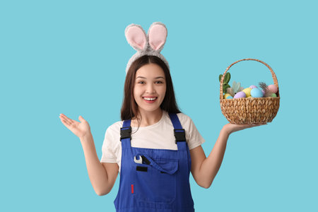 Female Asian worker in bunny ears with Easter eggs on blue background
